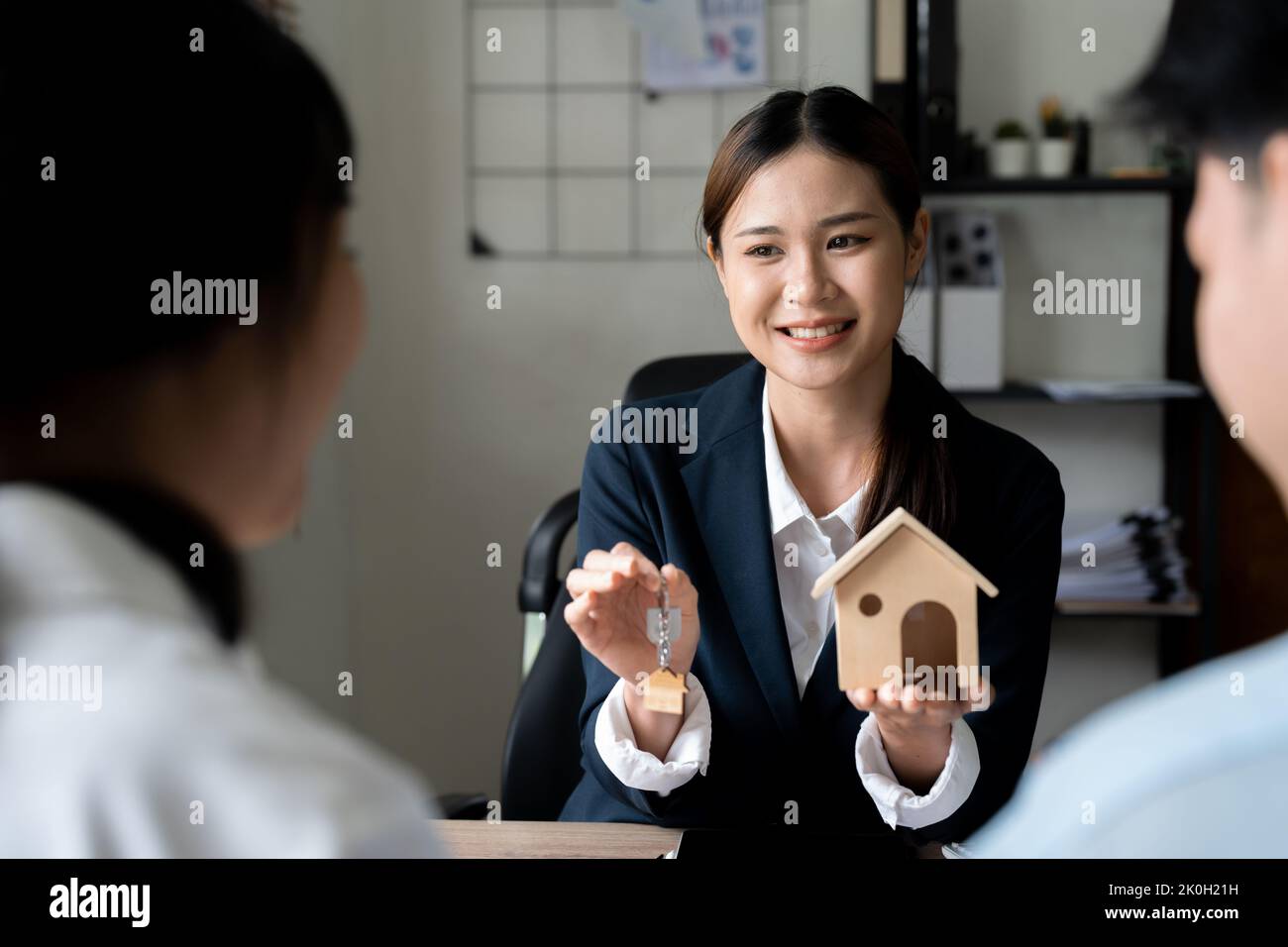 Coppia di famiglia felice che fa l'acquisto la loro prima casa, prendendo la chiave dal realtor femminile. Vista da dietro i clienti. Concetto di agenzia immobiliare Foto Stock