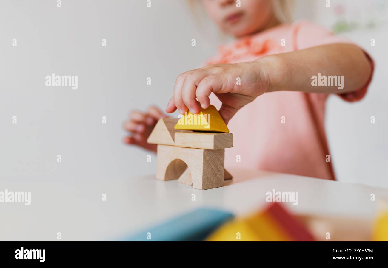 Bambina che gioca a blocchi di legno a casa o asilo. Concetto di sviluppo e costruzione. Mattoni educativi multicolore per l'apprendimento precoce e l'istruzione per i bambini piccoli. Foto Stock