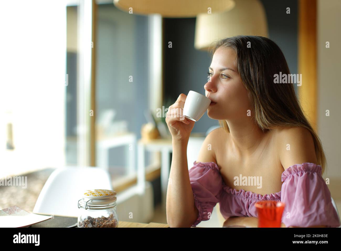 Giovane donna che beve caffè guardando though una finestra in un ristorante Foto Stock