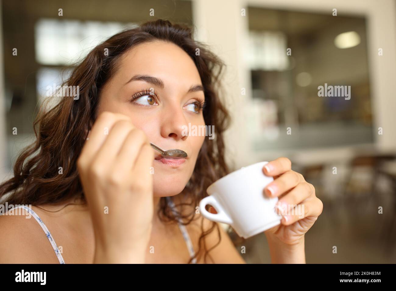 Donna che beve caffè usando il cucchiaio in un bar che guarda lontano Foto Stock
