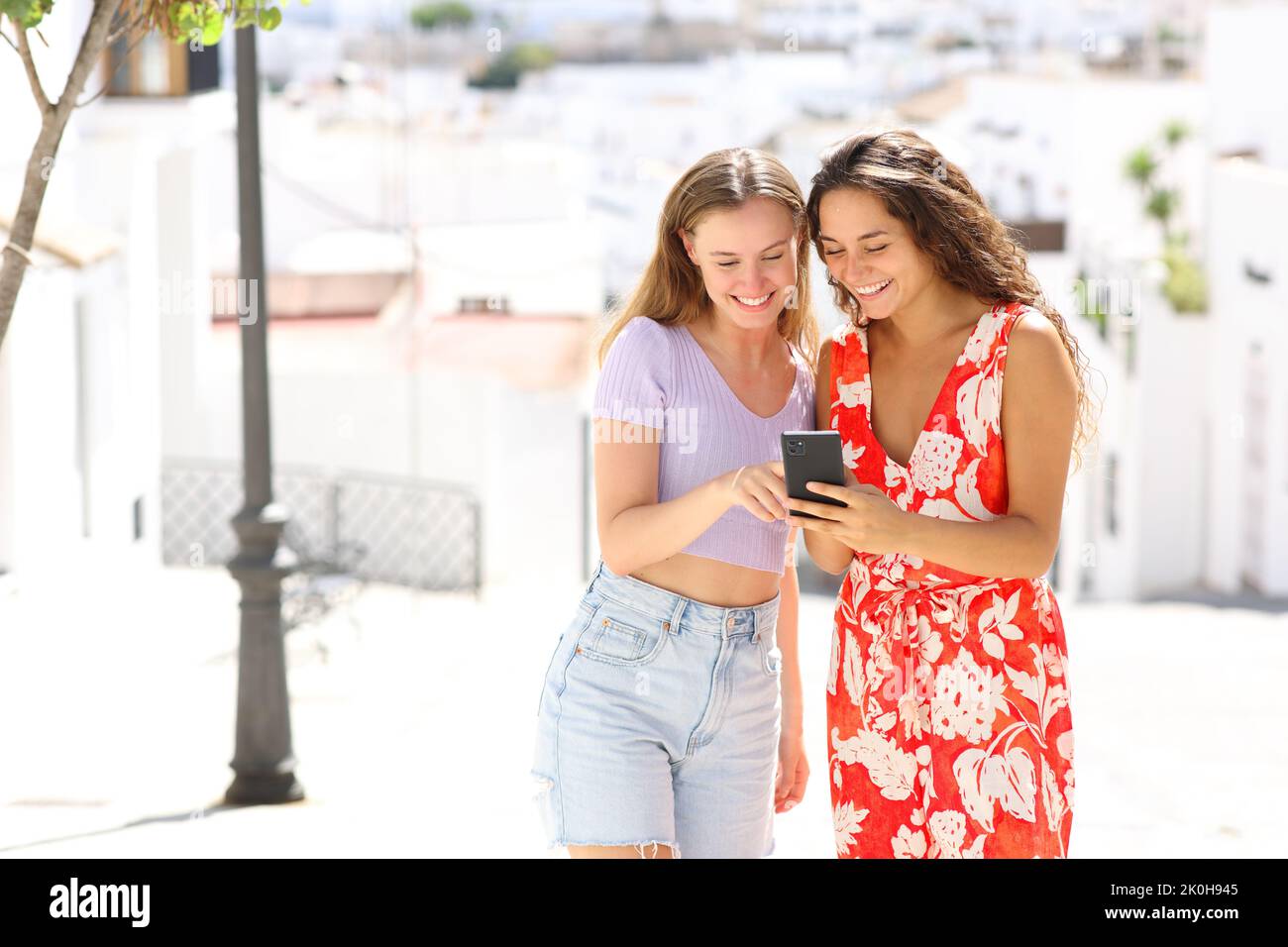 Turisti felici in una strada cittadina bianca che controlla lo smartphone durante le vacanze estive Foto Stock