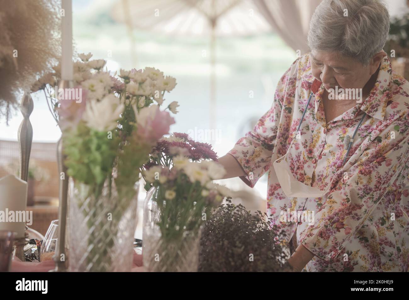 vecchia donna decorare bouquet di fiori in vaso di vetro sul tavolo da pranzo Foto Stock