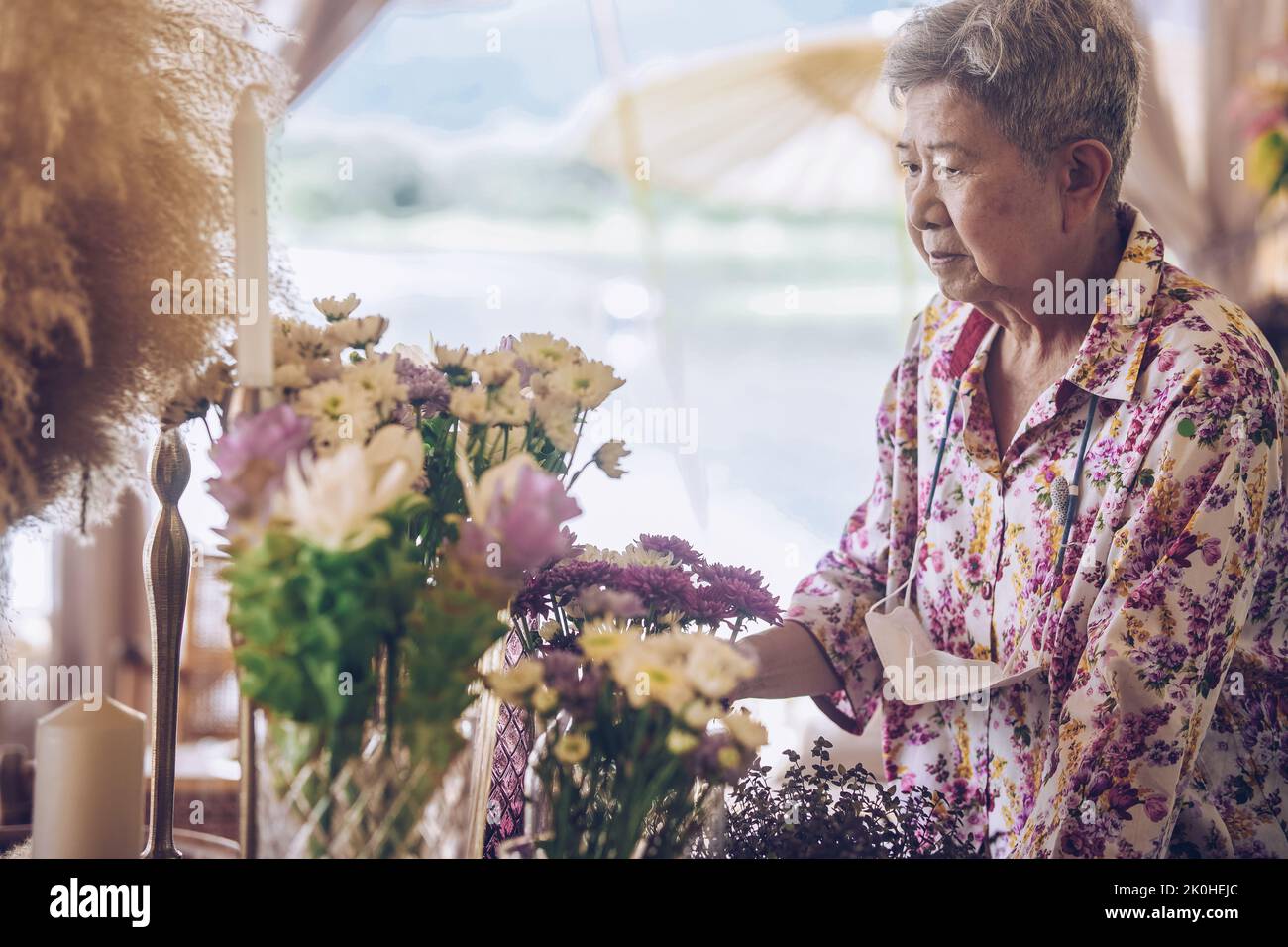 vecchia donna decorare bouquet di fiori in vaso di vetro sul tavolo da pranzo Foto Stock