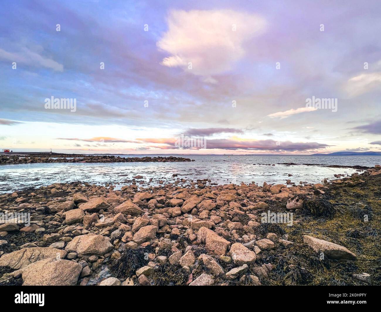 La splendida vista sul mare con spiaggia rocciosa a Salthill Promenade Galway, Irlanda sotto il cielo colorato tramonto nuvoloso Foto Stock