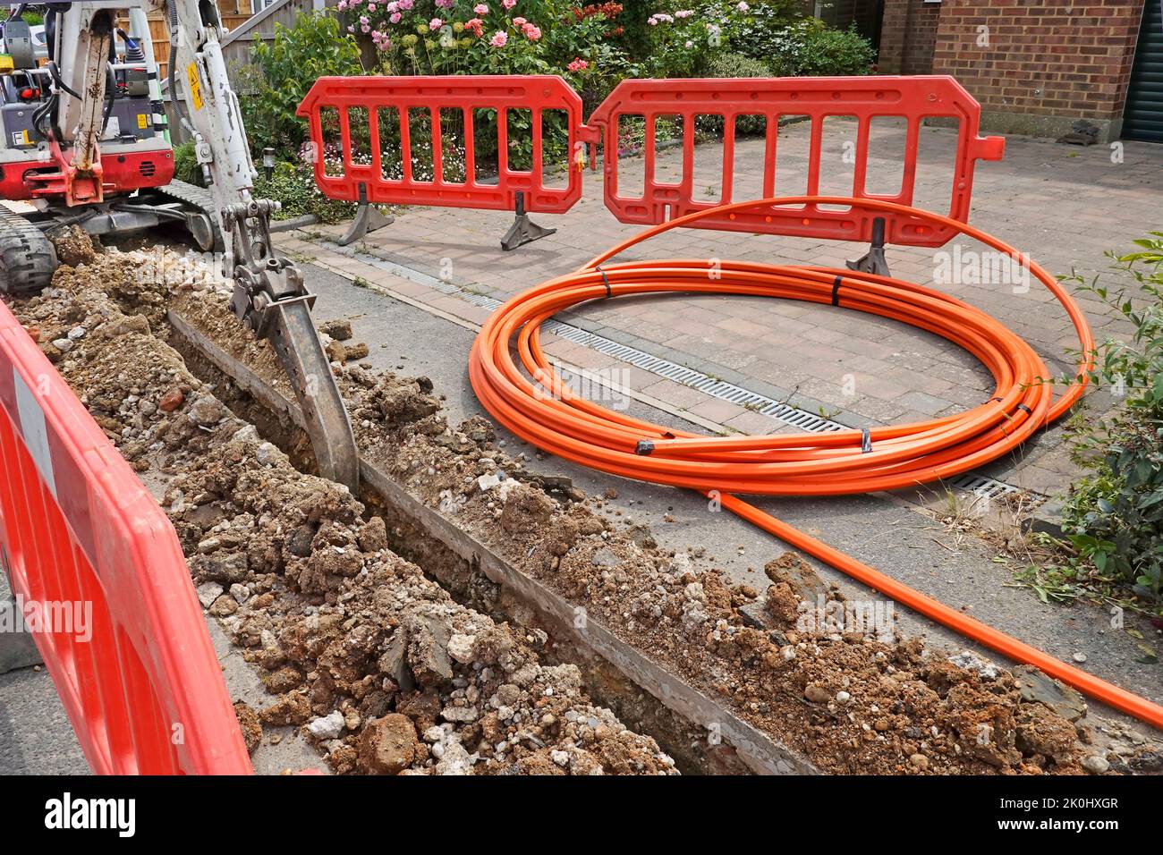 Mini scavatore posteriore macchina attrice scavatore canale stretto in pavimentazione per cavo a banda larga in fibra arancione avvolto chiuso casa chiusa vialetto Inghilterra UK Foto Stock