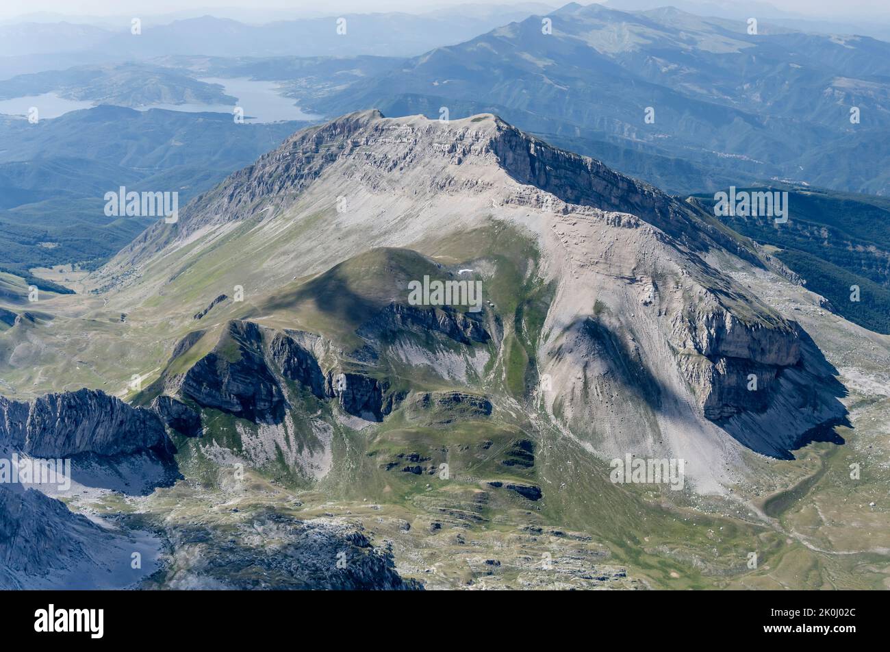 Ripresa aerea, da un piccolo aereo, con le brulicanti falesie del picco del Corvo nella gamma del Gran Sasso con il lago Campotosto sullo sfondo, ripresa da sud-ovest in risata Foto Stock