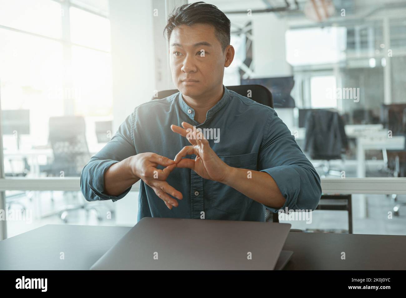 Uomo d'affari asiatico che usa il linguaggio dei segni con colleghi e amici mentre si siede in ufficio Foto Stock