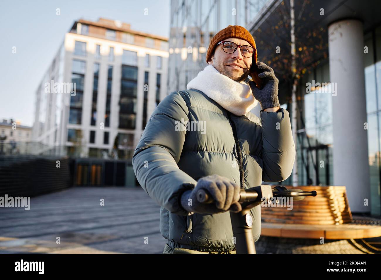 Giovane uomo che ha una conversazione sul telefono cellulare durante la guida in scooter lungo la strada nel giorno d'autunno Foto Stock