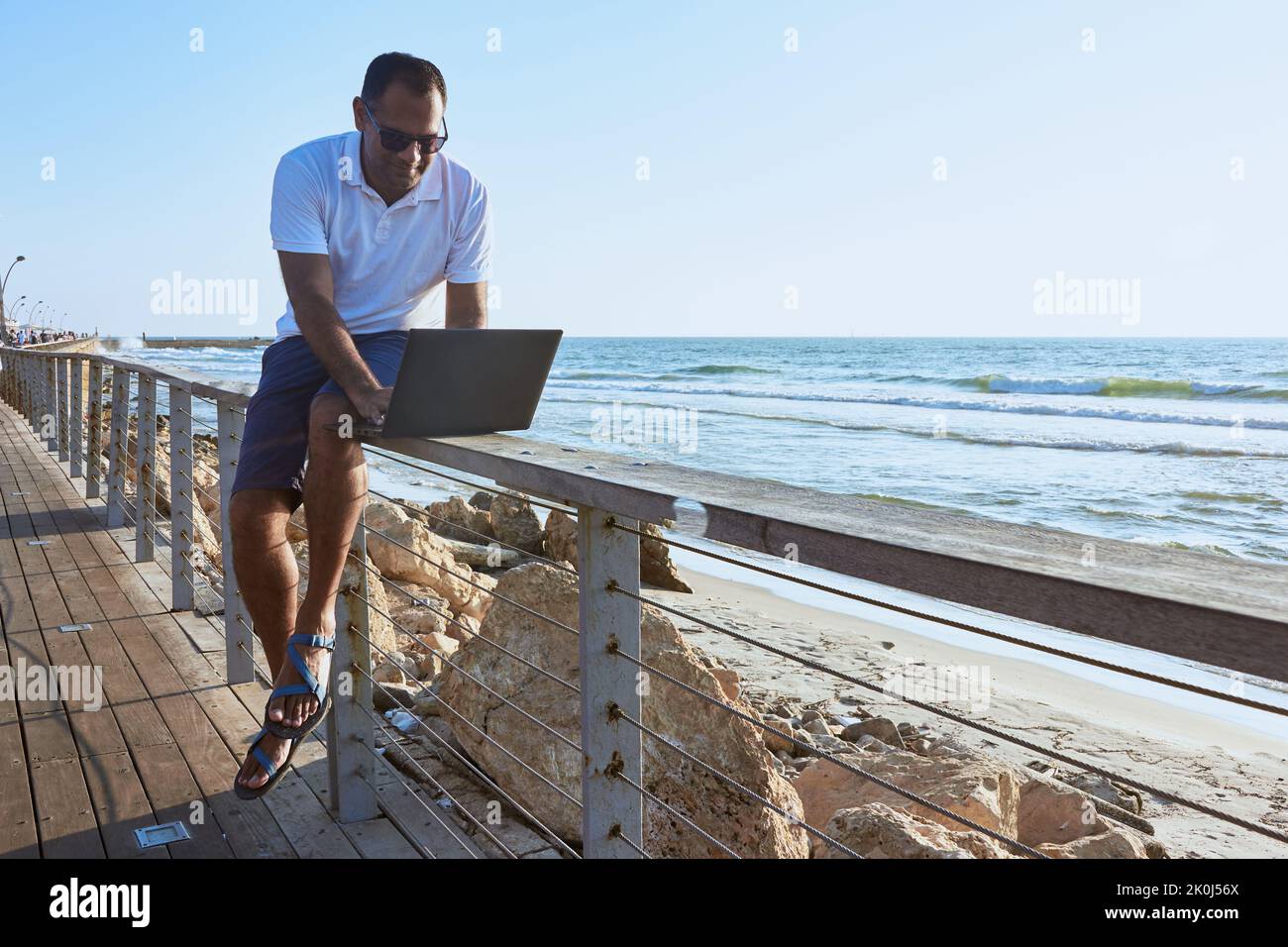 uomo che lavora su un computer portatile in remoto dalla spiaggia Foto Stock