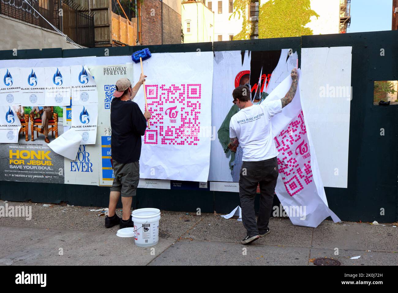 Persone che sbatte poster pubblicitari su un muro, o pubblicità di pubblicazione selvaggia, come parte di una campagna di marketing urbano, a livello stradale, guerilla. Foto Stock