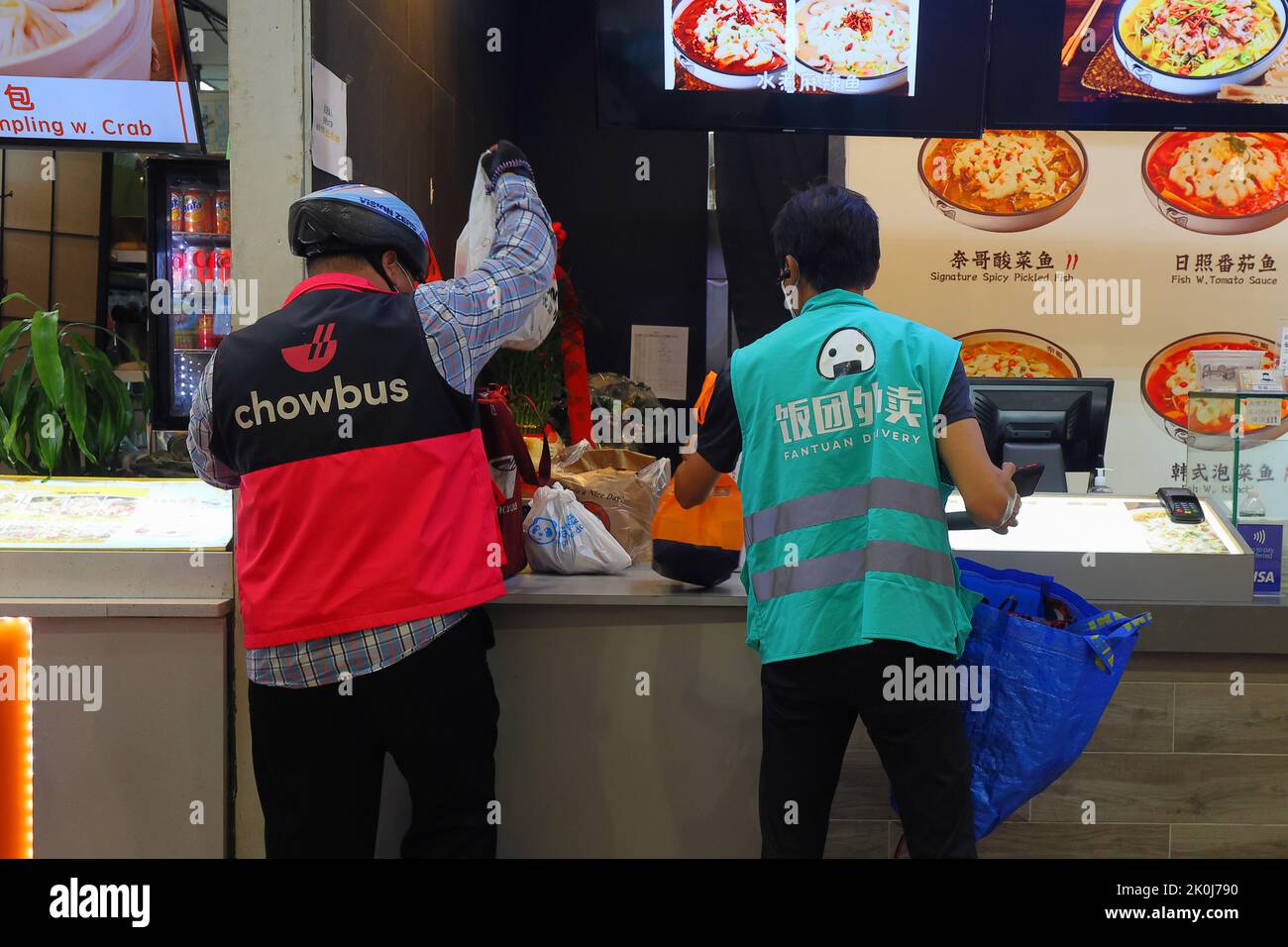 Un uomo di consegna di cibo di Chowbus ed una persona di consegna di Fantuan ritirano gli ordini cinesi di presa di alimento ad un tribunale di alimento in Downtown Flushing, New York. Foto Stock