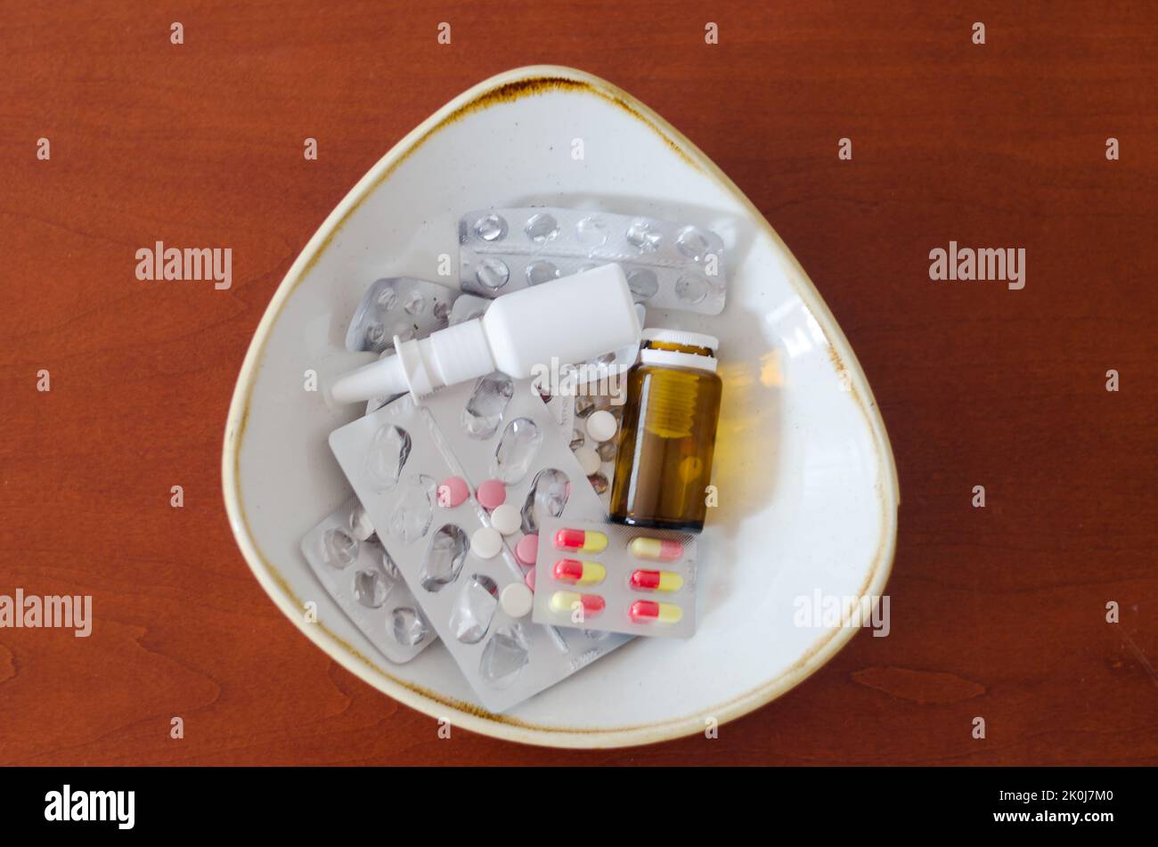 Molte pillole, gocce nel naso, confezioni e blister con pillole giacciono in un piatto sul tavolo. Sanità, industria medica. Stile di vita sano Foto Stock