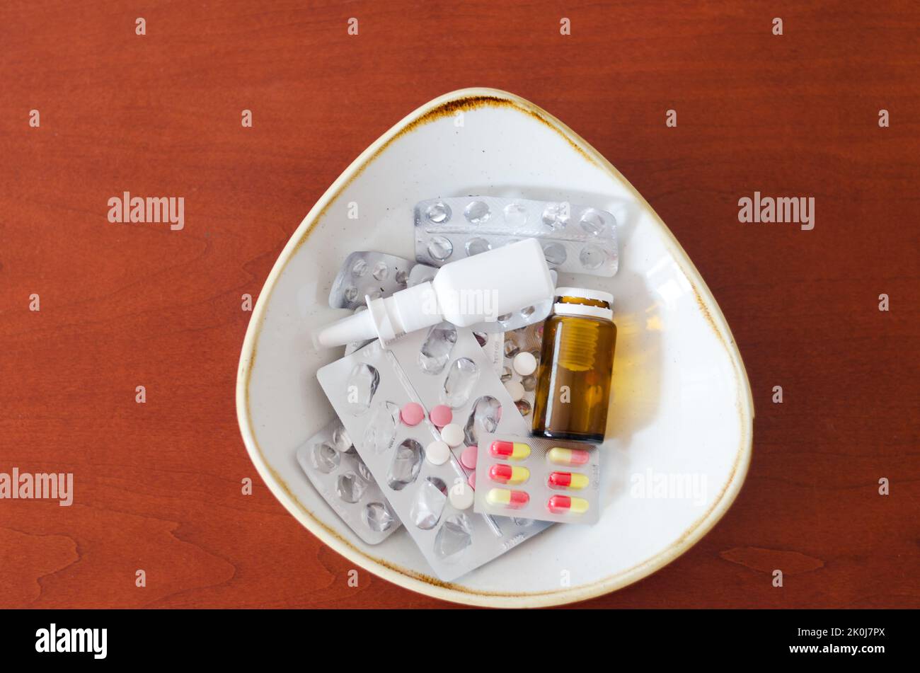 Molte pillole, gocce nel naso, confezioni e blister con pillole giacciono in un piatto sul tavolo. Sanità, industria medica. Stile di vita sano Foto Stock