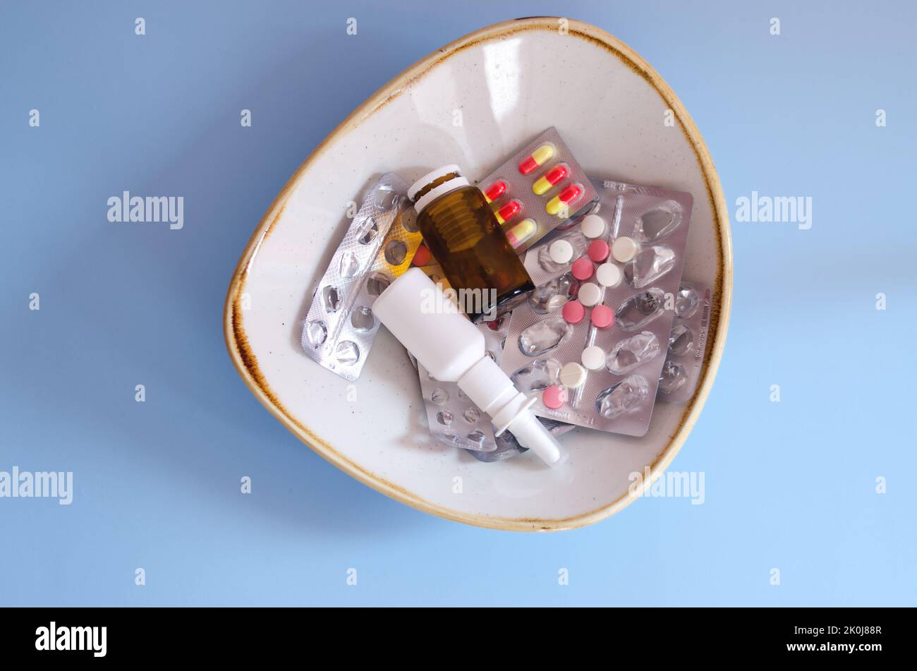 Molte pillole, gocce nel naso, confezioni e blister con pillole giacciono in un piatto sul tavolo. Sanità, industria medica. Stile di vita sano Foto Stock