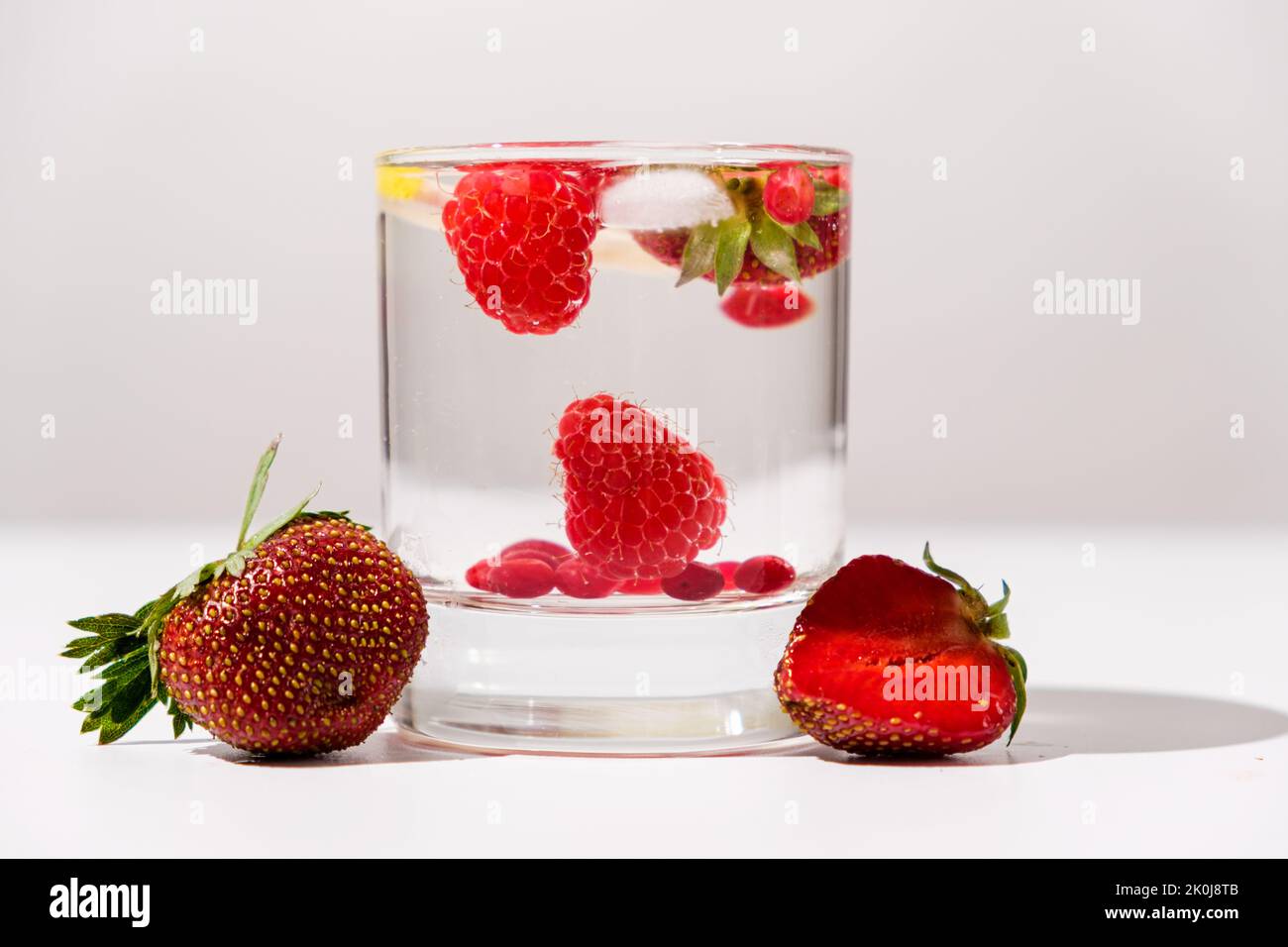 Cocktail estivo con fragole, lamponi e ghiaccio su sfondo bianco, vista laterale. Foto Stock