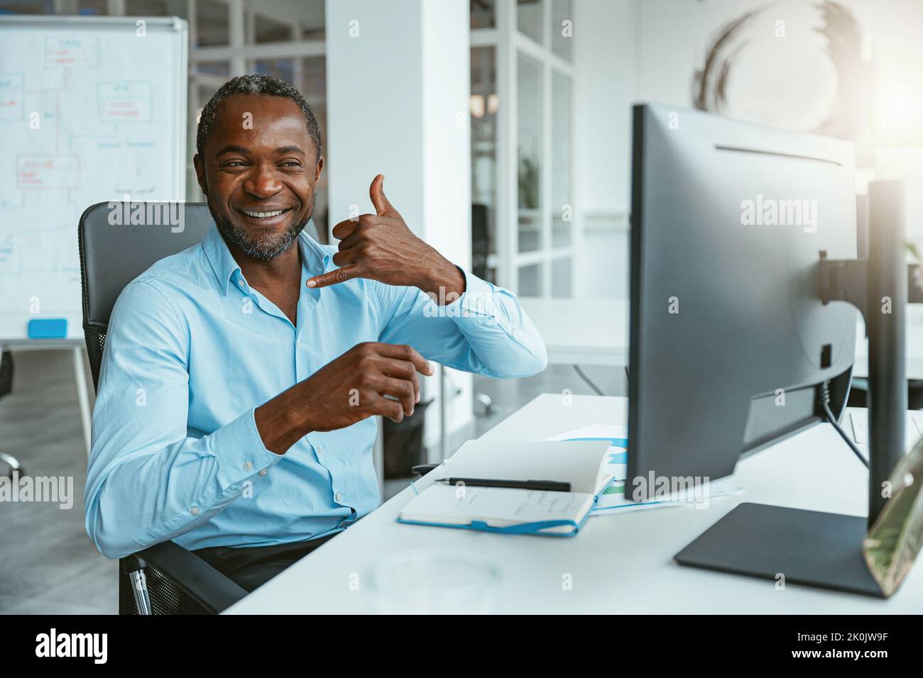 Uomo d'affari africano che usa il linguaggio dei segni mentre parla in linea con il cliente seduto in ufficio Foto Stock