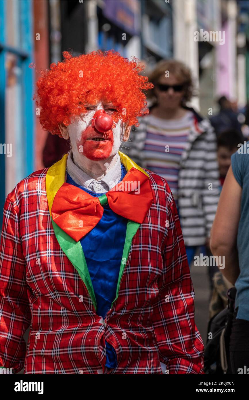 Un clown a piedi attraverso Penzance Pensans Town centro cercando inquisitivo. Foto Stock