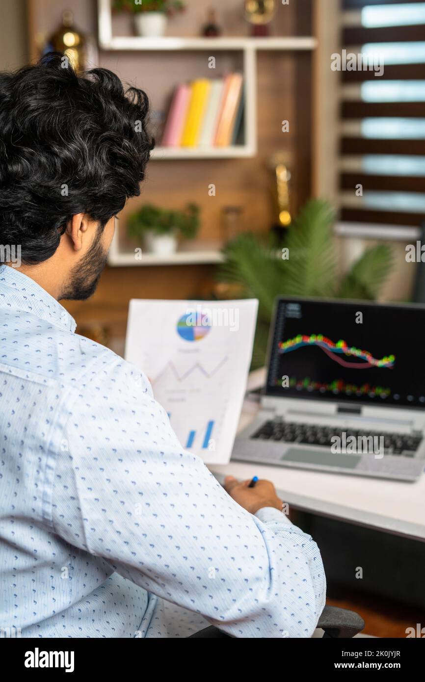 Immagine verticale di un giovane impegnato ad analizzare i grafici finanziari delle aziende con i grafici tecnici del magazzino sul laptop - concetto di investimento, commercio e. Foto Stock
