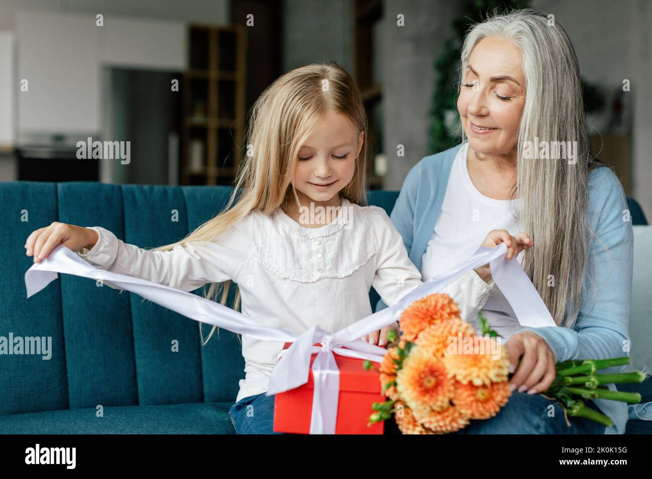 Felice nonna caucasica apre la scatola con il regalo della nonna anziana con bouquet di fiori Foto Stock