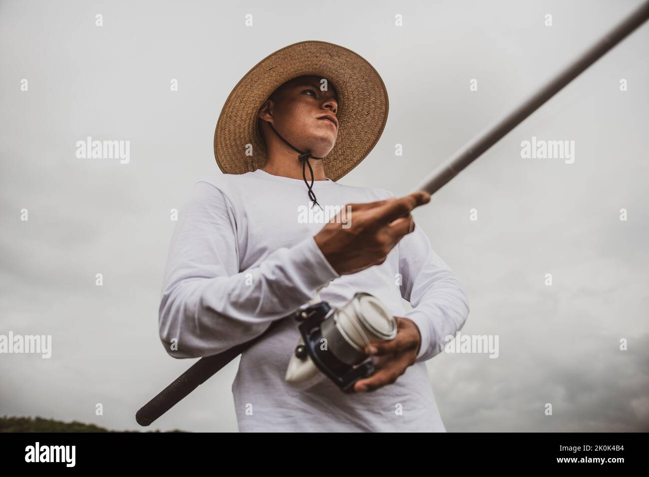 Da sotto maschio in cappello con canna da pesca cattura di pesce sulla riva sabbiosa Foto Stock