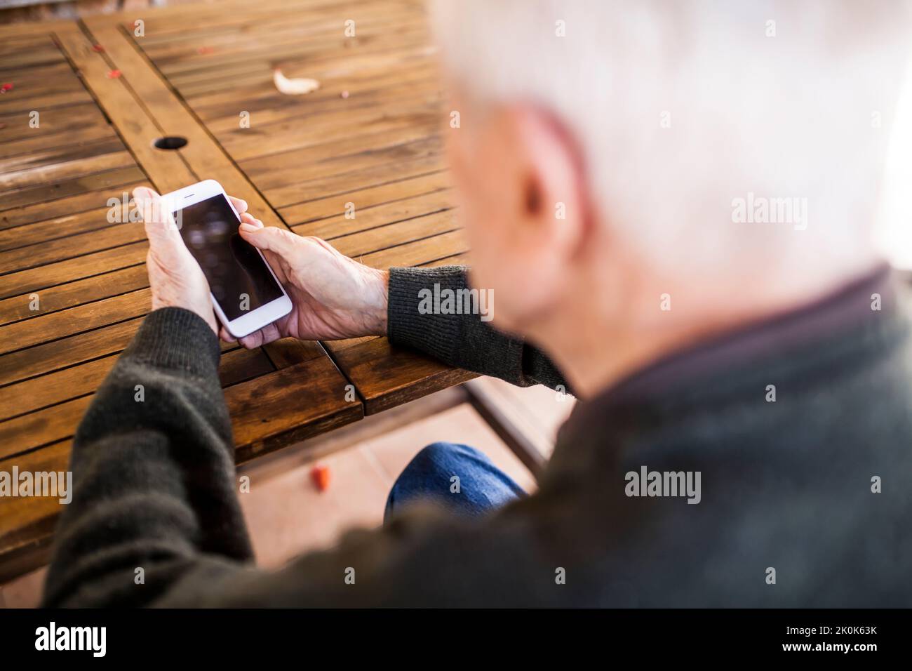 Uomo anziano che usa il suo smartphone seduto al tavolo di casa Foto Stock