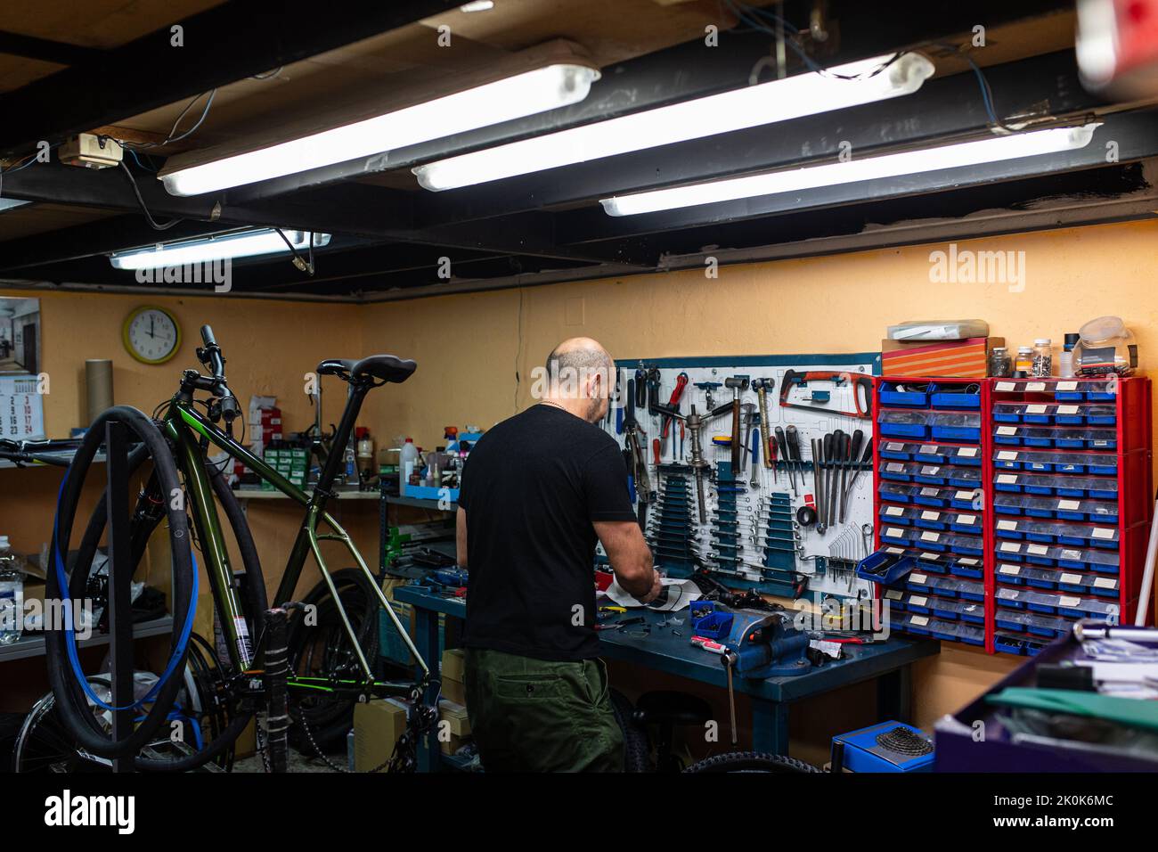Vista posteriore dell'uomo calvo in piedi vicino all'officina mentre fissa la bicicletta in un moderno garage professionale Foto Stock