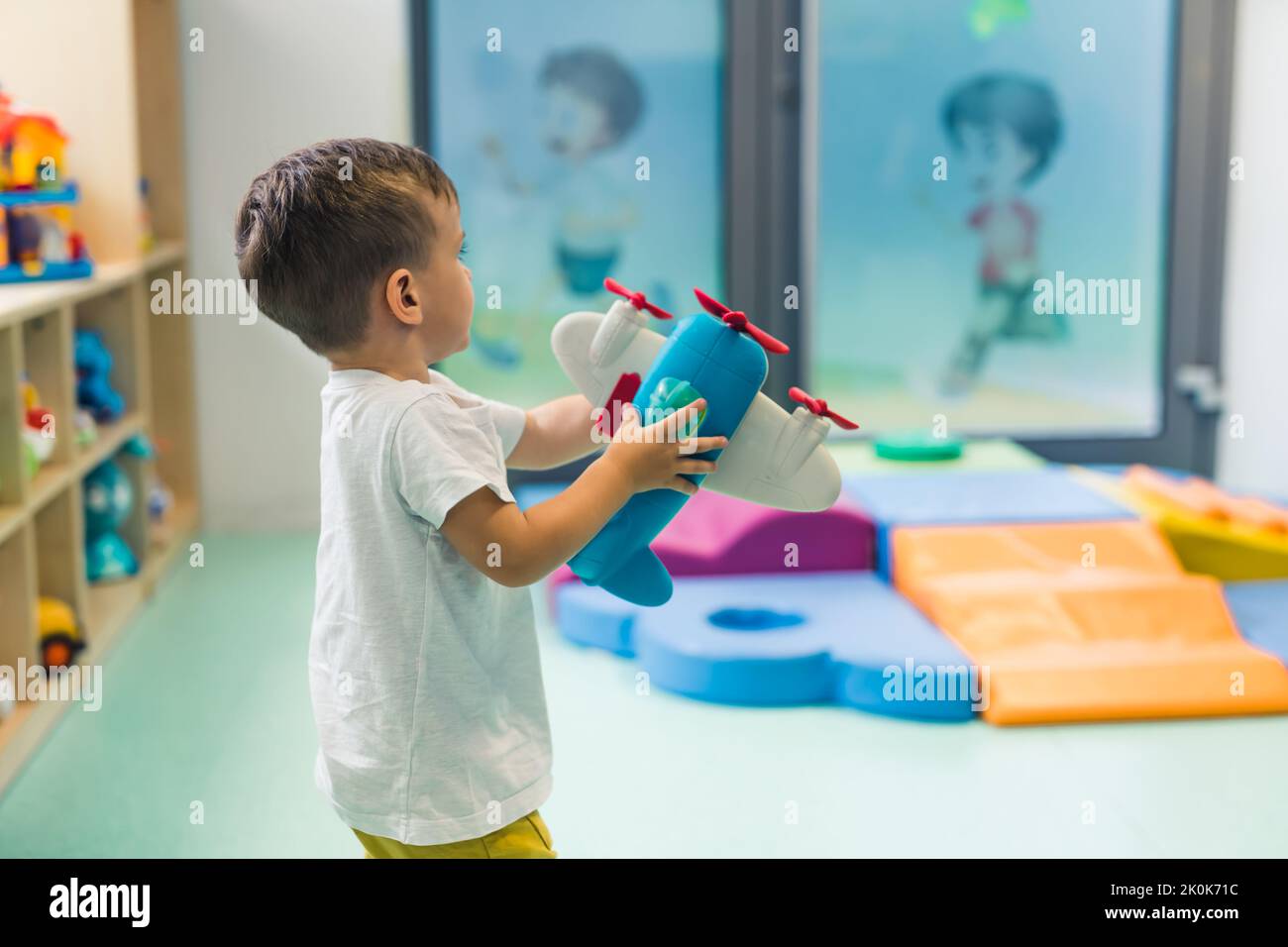 Immaginazione e sviluppo del pensiero creativo. Bambino che gioca con un giocattolo aereo in una stanza dei giochi della scuola materna. Foto di alta qualità Foto Stock