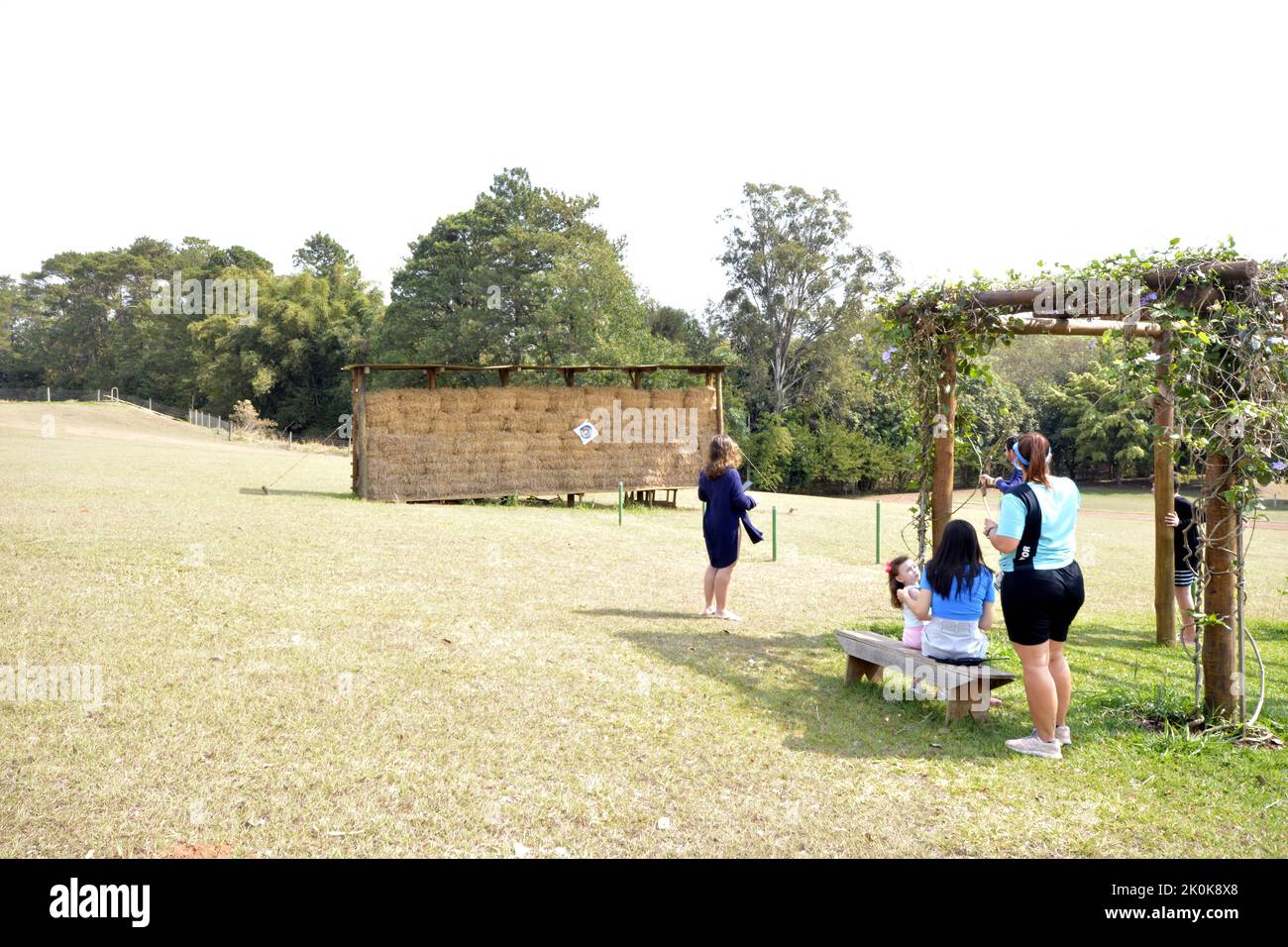 Turisti in una fattoria ecoturismo pratica tiro con l'arco con monitor di guardare. Città sfondo zona urbana. Panorama grandangolare. Cielo nuvoloso blu Foto Stock