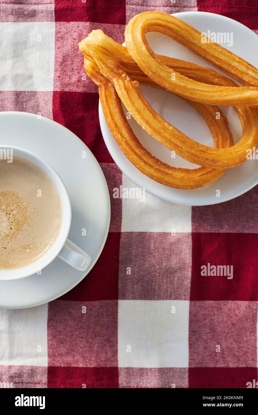 Churros appetitosi sul piatto e tazza di caffè fresco del mattino servito sul tovagliolo sul tavolo per la colazione in cucina Foto Stock