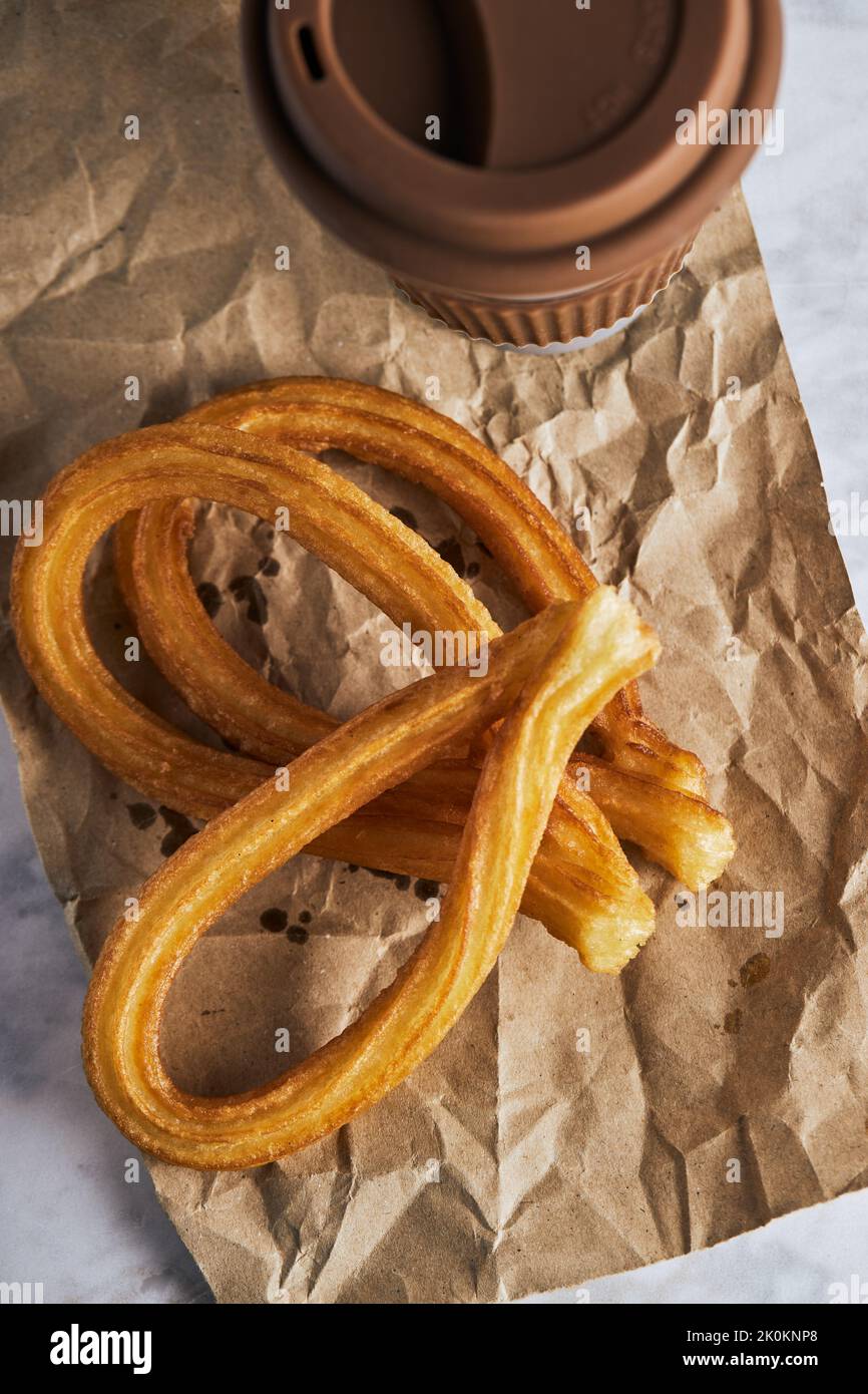 Churros croccanti freschi e tazza di caffè caldo posti sul tavolo per la colazione Foto Stock