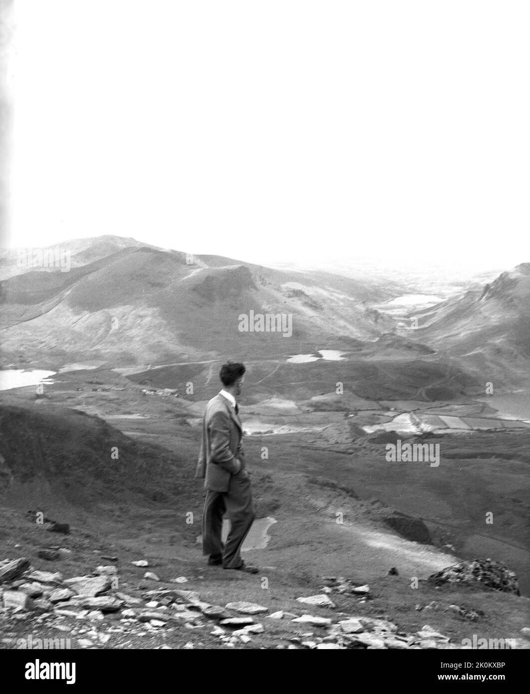 1956, storico, un uomo che indossa una giacca sportiva e pantaloni che si trova ad un alto livello nel parco nazionale di Snowdonia, Galles, Regno Unito, e guarda la catena montuosa, la valle e il paesaggio sottostante. Foto Stock