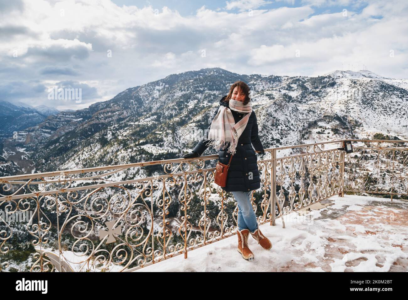 Giovane donna in piedi sul ponte di osservazione della montagna sopra la gola di Vouraikos. Mega Spileon Monastero terrazza con splendida vista sulle montagne innevate. Vacanze invernali. Grecia Foto Stock