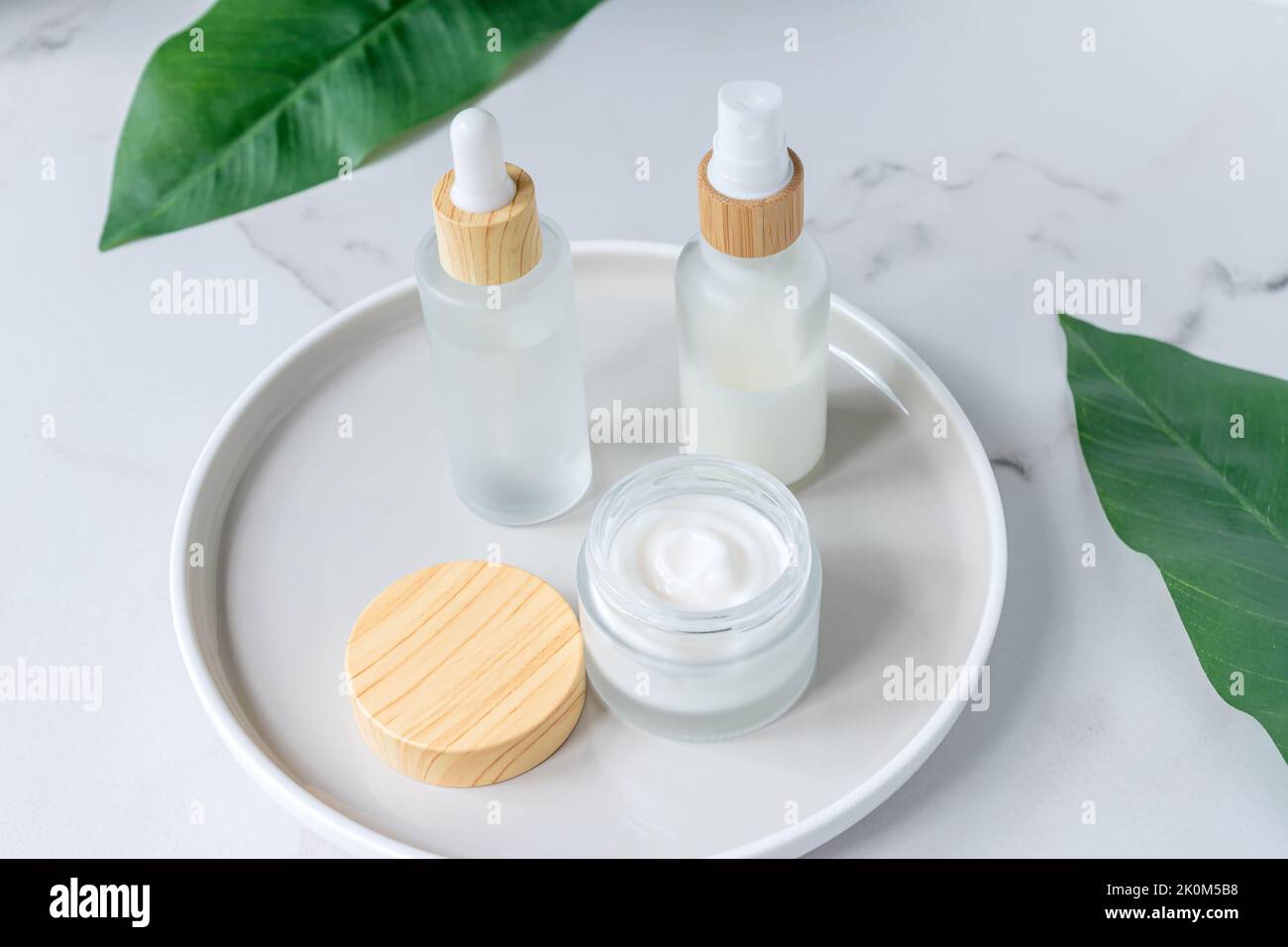 Confezione cosmetica con foglie di erbe verdi. Set di bottiglie cosmetiche di crema o lozione su sfondo marmoreo. Confezione vuota. Centro termale di bellezza naturale pro Foto Stock