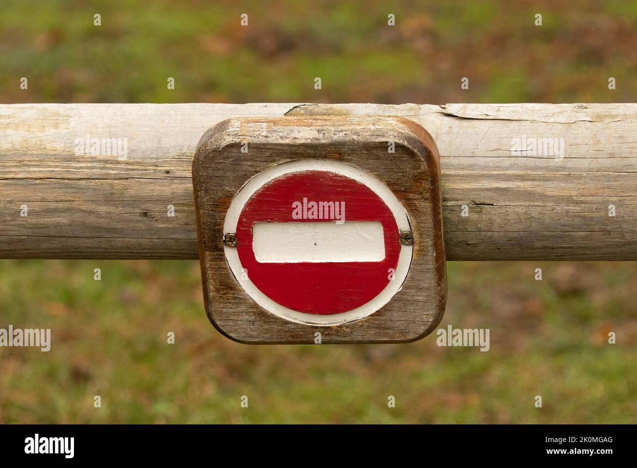 Primo piano di un cartello No Entry in forma di cerchio rosso con una linea bianca sul palo di legno, sfondo sfocato Foto Stock