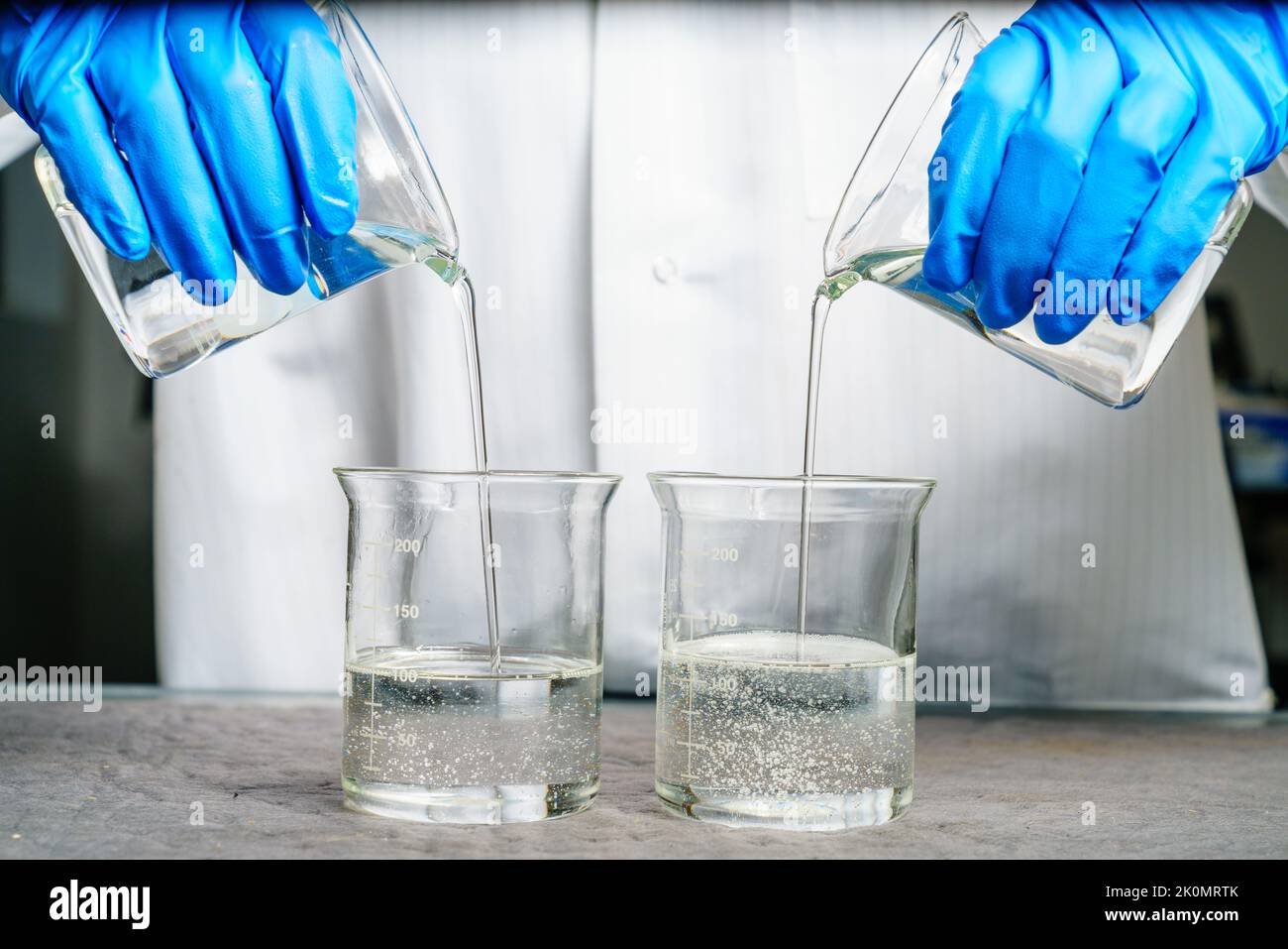 Una persona in un camice da laboratorio versa due liquidi trasparenti nei becher Foto Stock