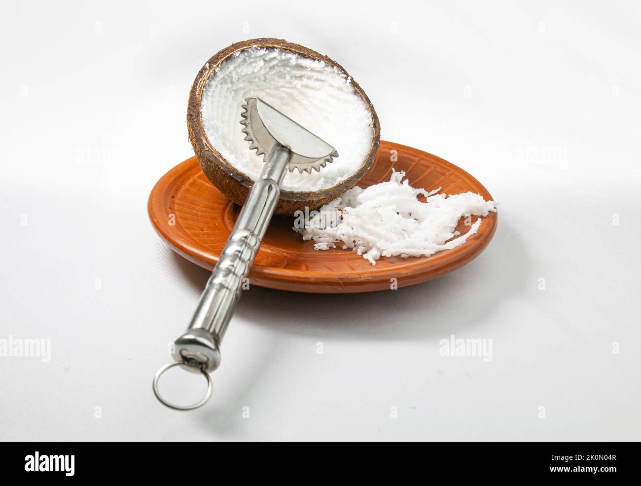 Cocco grattugiato in un piatto di fango con una grattugia a mano di cocco su sfondo bianco. Foto Stock