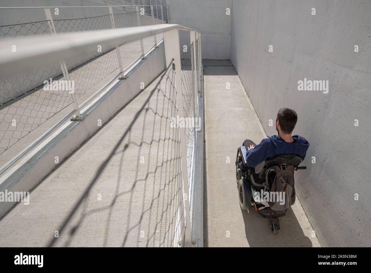 Uomo su sedia a rotelle, in avvicinamento all'edificio che si sposta lungo una rampa accessibile per persone con disabilità Foto Stock