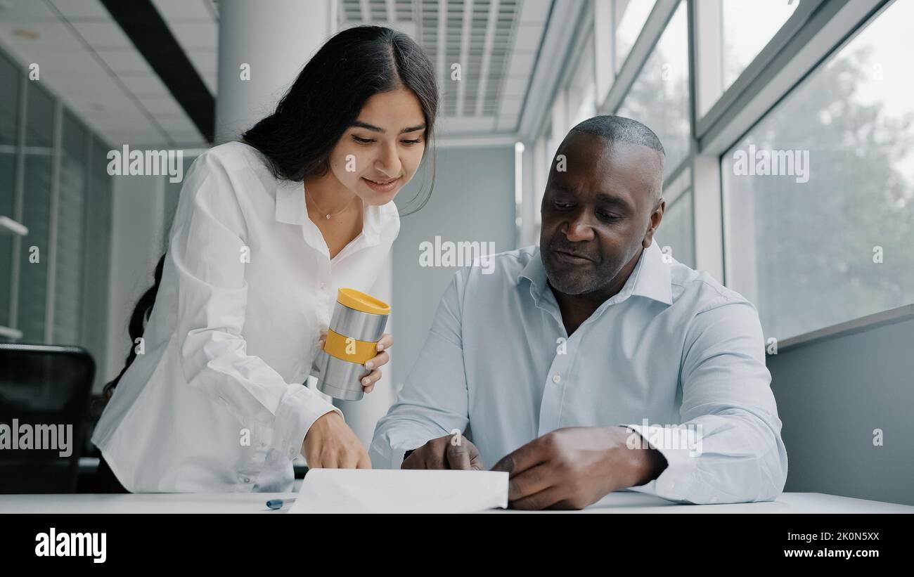 Due colleghi partner aziendali colleghi di ufficio analizzano le informazioni relative al controllo dei documenti cartacei. Donna araba controllare documentazione documenti rapporto aiutare africano Foto Stock