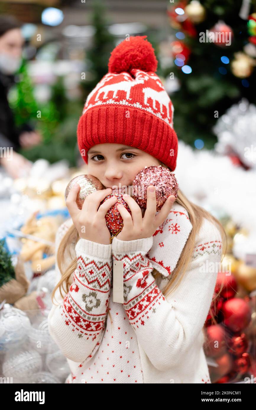 Una ragazza carina in un cappello rosso di Natale in un centro commerciale sceglie i regali per Natale e Capodanno e sorride dolcemente. Il concetto di una vacanza, shopping, sconti il Black Friday. Foto Stock