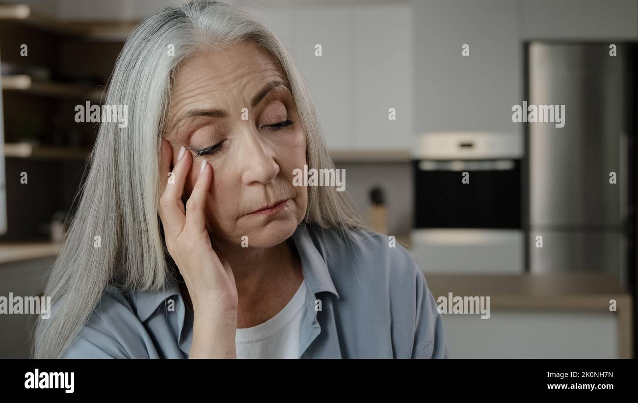 Deluso triste anziano donna caucasica grigio-capelli signora maturo miserabile donna tenere mano sulla testa massaggiare tempio sentire malessere problema di salute alto Foto Stock