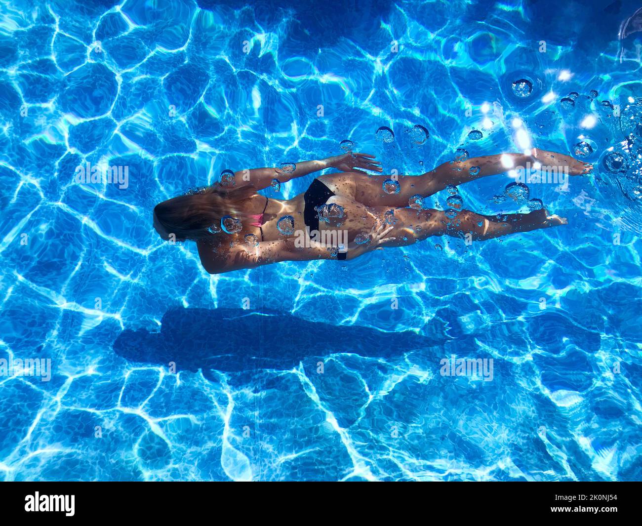 Vista ad alto angolo della donna che nuota sott'acqua in una piscina all'aperto di colore blu luminoso in una giornata di sole Foto Stock