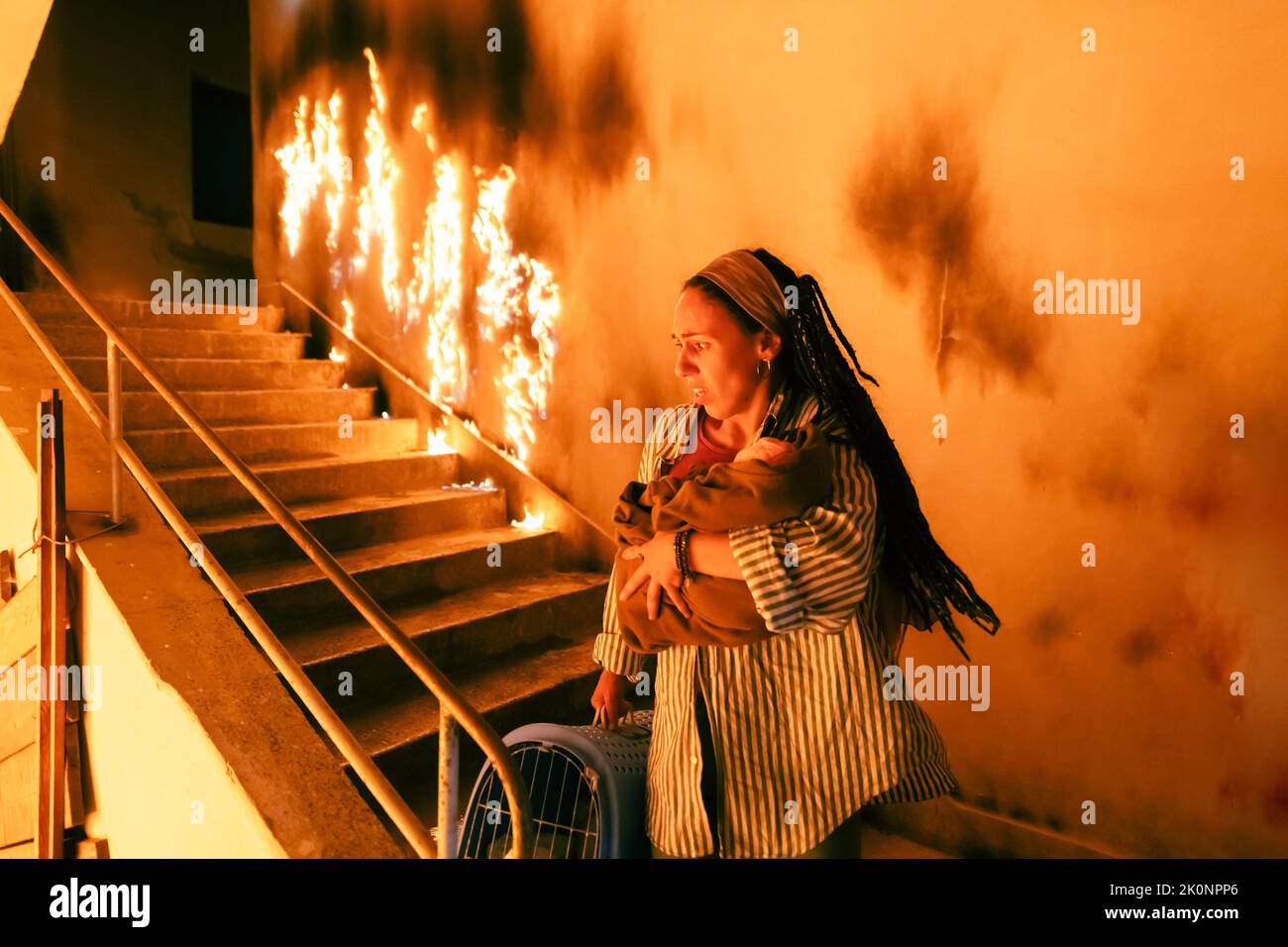 Il Fireman coraggioso scende le scale di un edificio che brucia e tiene la ragazza salvata nelle sue braccia. Fuoco aperto e un pompiere in background. Foto Stock