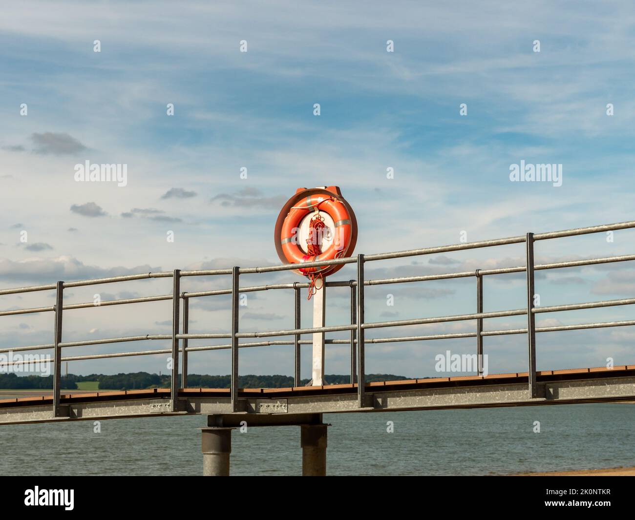 Cintura di sicurezza su un molo. Anello di sicurezza rosso quando una persona ha bisogno di aiuto. Attrezzatura per il salvataggio di persone in acqua. Edificio sul mare in Germania. Foto Stock