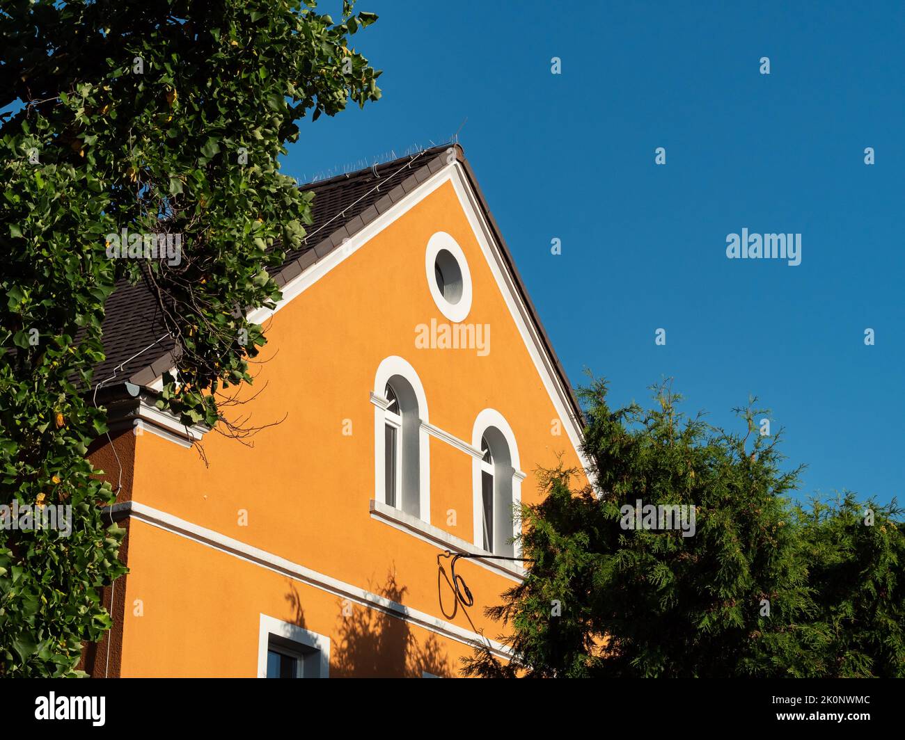 Una facciata casa tedesca tra le corone verdi dell'albero. Vecchio edificio esterno con un tetto a timpano di fronte ad un cielo blu. Architettura antica in Germania. Foto Stock