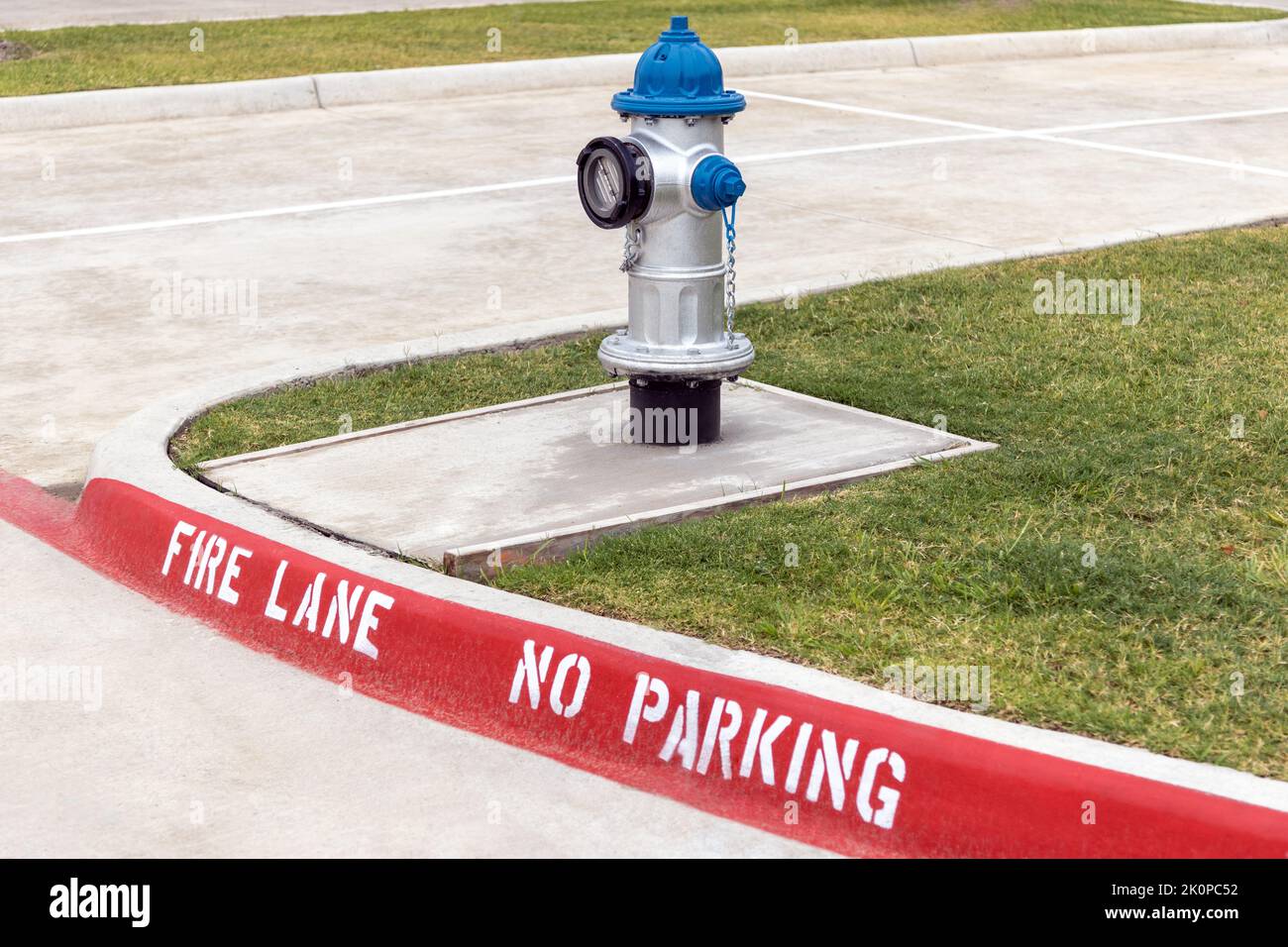 Idrante antincendio grigio e blu sul marciapiede, corsia antincendio rossa senza contrassegno di parcheggio sul marciapiede della strada Foto Stock