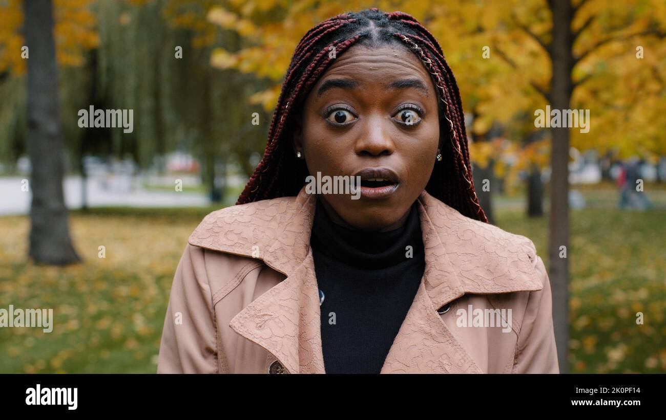 Primo piano stordito afro-americano donna in piedi all'aperto guardando la fotocamera con gli occhi spalancati e la bocca sensazione shock sorpresa da notizie inaspettate Foto Stock