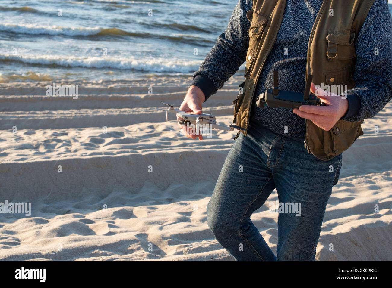 Nida, Lituania - 9.12.2022: Uomo con telecomando drone e Drone Dji mavic mini. Ripresa ritagliata, primo piano. Foto Stock