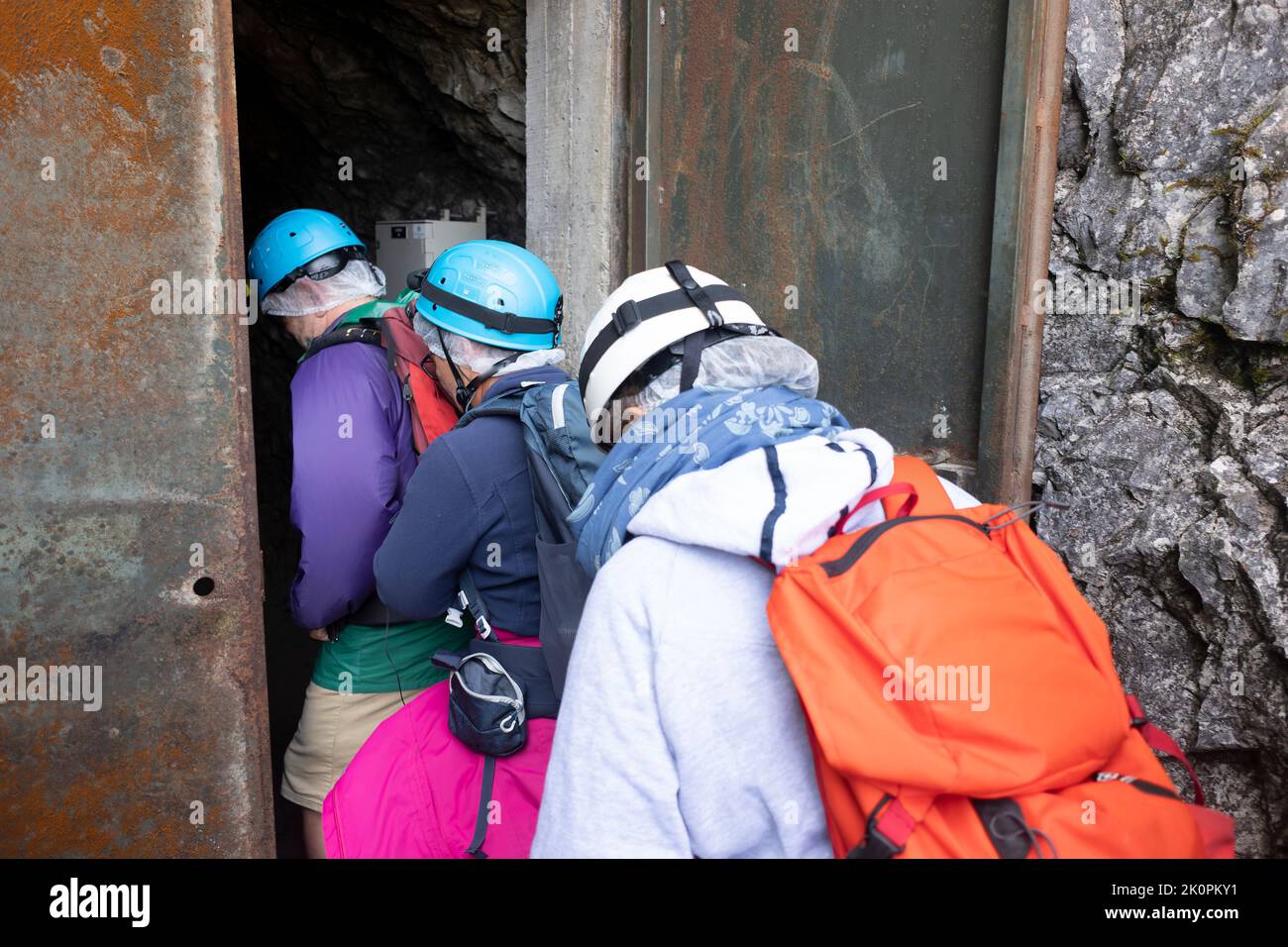 Tre anziani non identificati entrano nella grotta per andare a speleologia. Vestito con abiti speciali ed elementi di sicurezza, casco, abiti caldi. Foto Stock