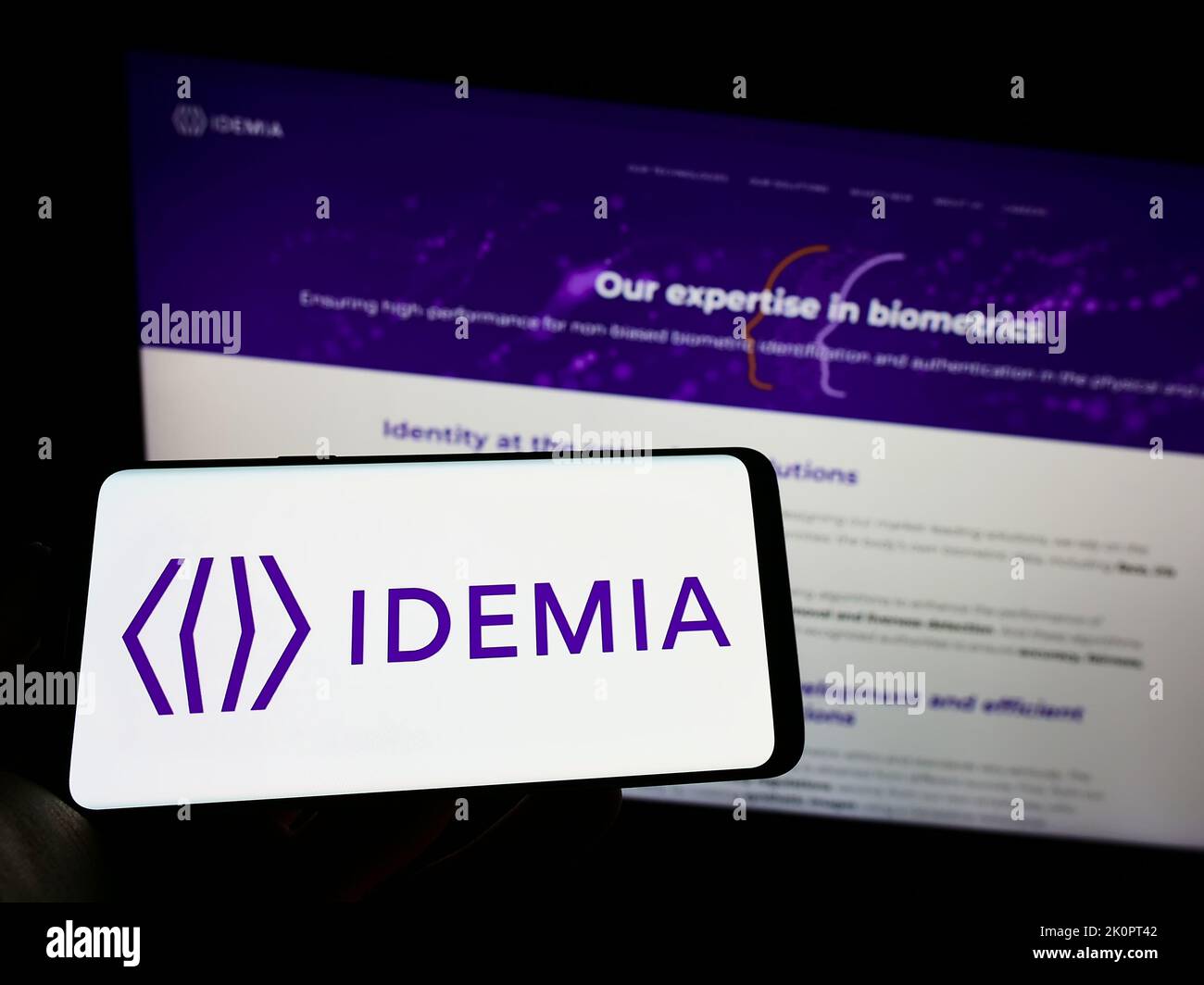 Persona che tiene il cellulare con il logo della società di tecnologia IDEMIA France SAS sullo schermo di fronte al sito web aziendale. Messa a fuoco sul display del telefono. Foto Stock