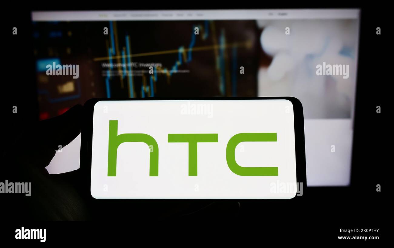 Persona che tiene un telefono cellulare con il logo della società di elettronica taiwanese HTC Corporation sullo schermo davanti alla pagina web. Messa a fuoco sul display del telefono. Foto Stock